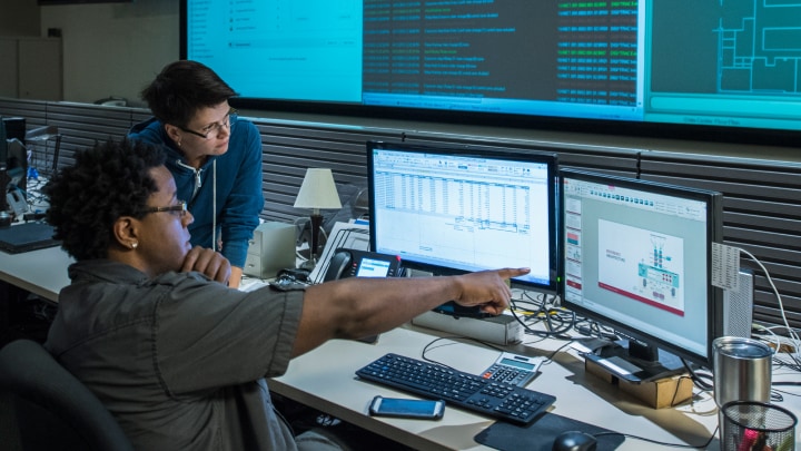 Two people working on multiple computer screens
