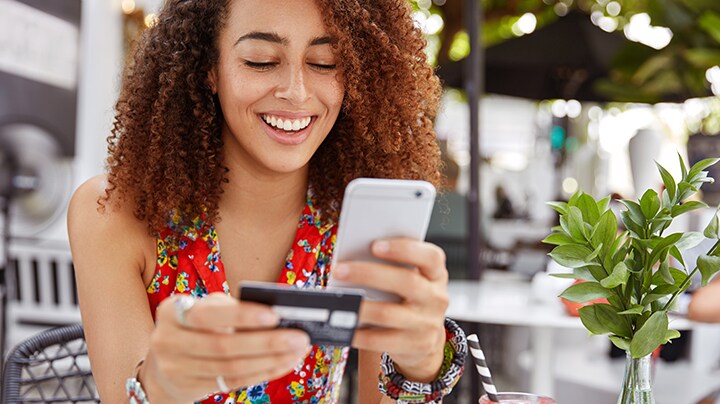 A person looking at a mobile phone and holding a credit card